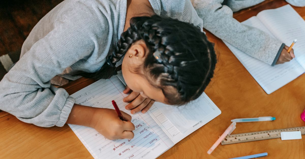 From above of focused kids writing in copybooks while doing homework together at wooden table